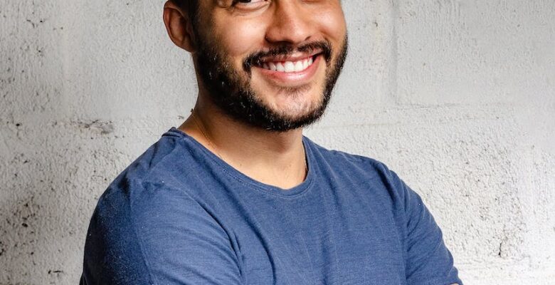 portrait photo of smiling man with his arms crossed standing in front of white wall