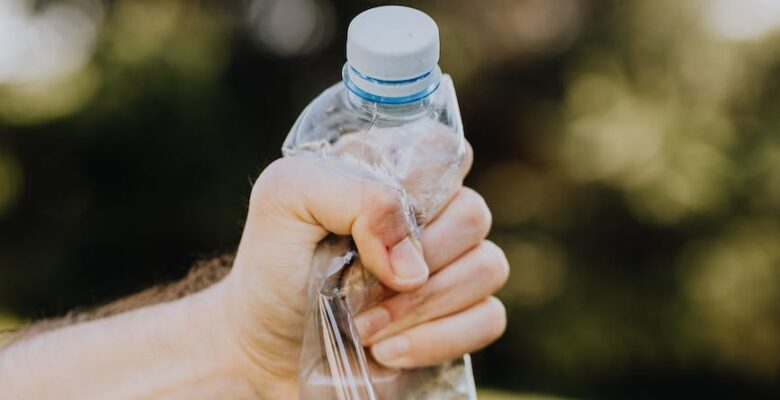 crop male crushing plastic water bottle in park