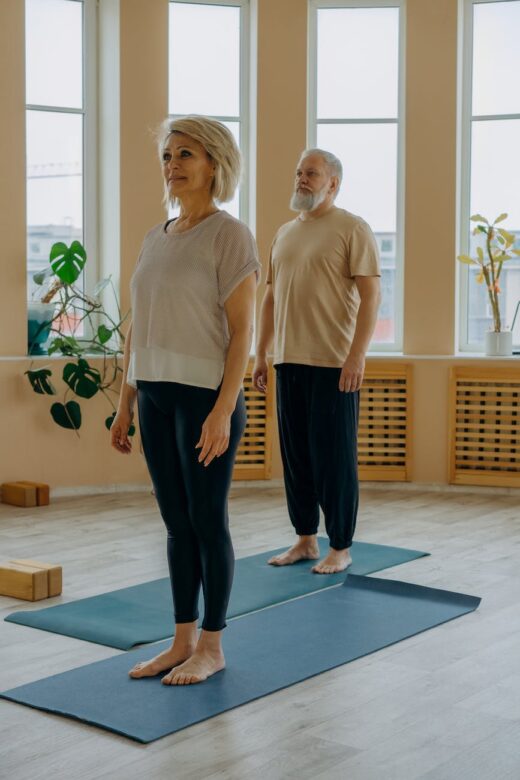 an elderly man and woman standing on a yoga mat