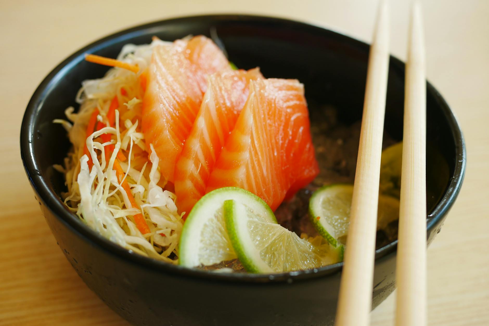 slices of salmon sashimi with slices of lime on black bowl